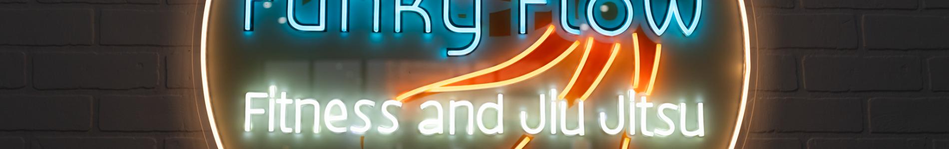 Neon sign for “Funky Flow Fitness and Jiu Jitsu” featuring a stylized orange octopus inside a glowing circle on a brick wall