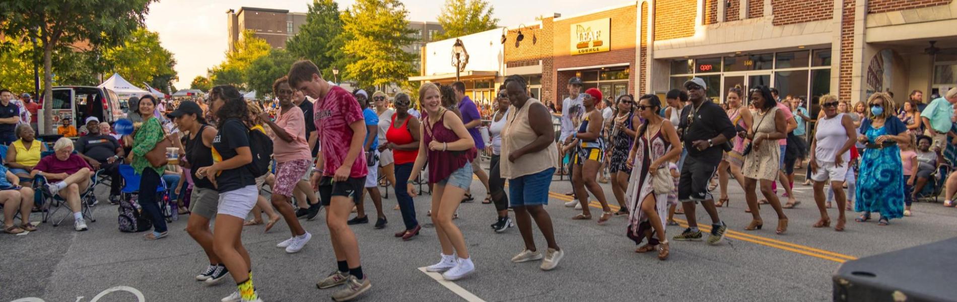 A diverse crowd dancing in the street on a sunny day.