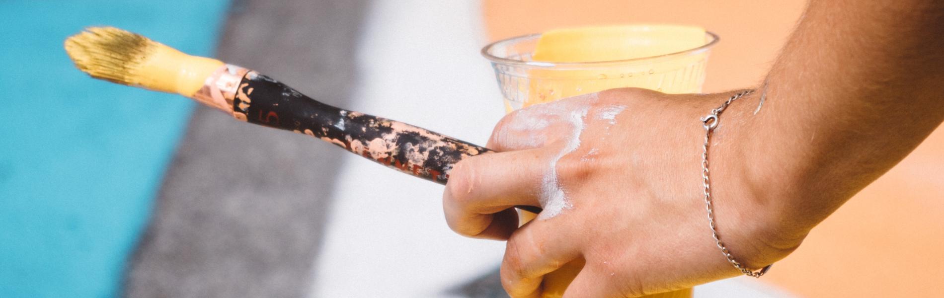 Person holding a paint brush and paint cup above a mural