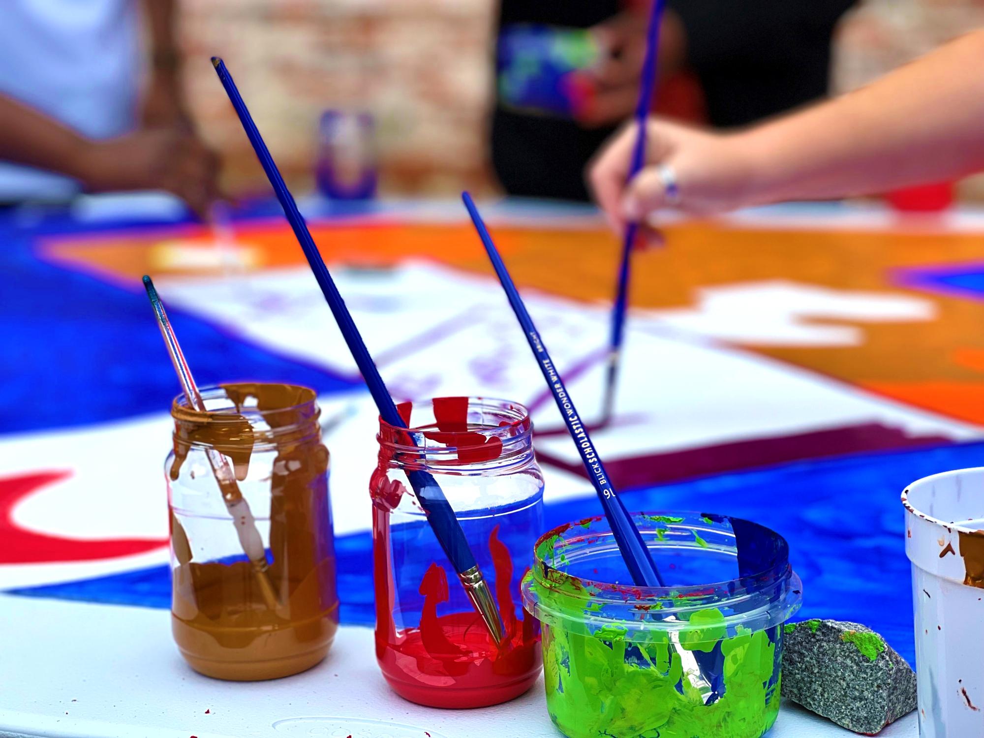 Two individuals painting on a tabletop surface.